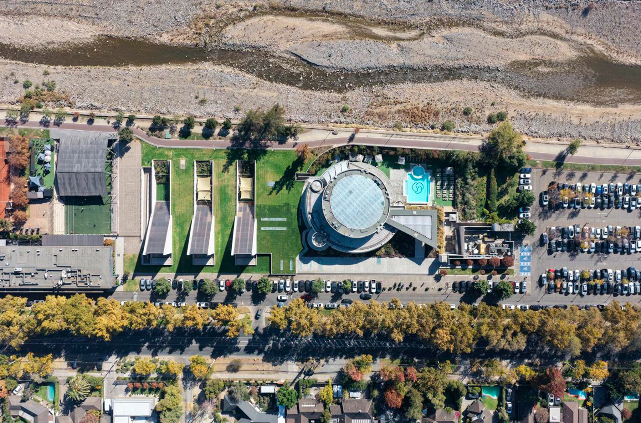 Vista aérea de Club Balthus junto al río Mapocho, Chile, con volumen circular y áreas deportivas